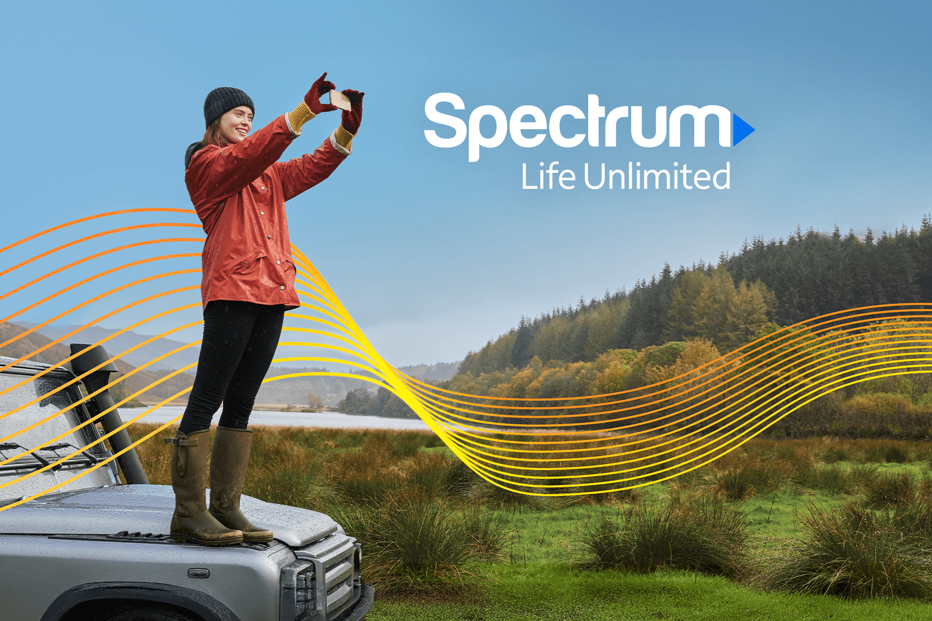 Woman standing on hood of car taking a photo of a mountain range